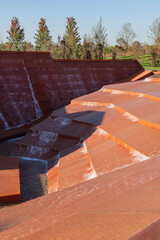 Modern cascading water feature with geometric, rust-colored concrete steps and flowing water. Water amphitheater or canyon in Krasnodar's city park, or Galitsky Park.