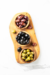 Olives in wooden bowls and Olive oil in the bottle at white table.