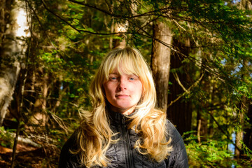 Young woman with flowing blond hair with highlights head and shoulders facing camera boreal forest background