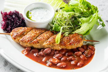 A vibrant plate featuring grilled lyulya kebab served with red kidney beans in tomato sauce, a...