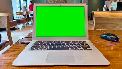 Laptop on Table with Green Screen: A modern laptop with a vibrant green screen sits prominently on a wooden table, suggesting endless possibilities for display or work.