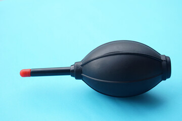 A black rubber air blower with a red tip placed on light blue background, commonly used for cleaning cameras and delicate electronics. Concept electronic equipment care tool for removing dust on lens.