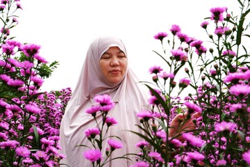 Warm portrait of a woman standing among pink flowers under bright daylight.