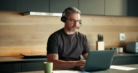 Online, headset and man with laptop in kitchen, virtual assistant and financial analysis on website. Talking, mature person and communication with contact in home, remote work and risk management - Powered by Adobe