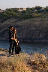 Romantic couple standing on a cliff above the river at sunset