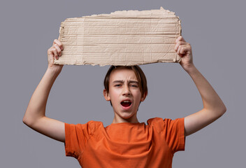 Protest. Little cute boy kid holding cardboard banner with blank space annoyed, frustrated shouting with anger, yelling crazy with anger. Young man holding blank empty banner, gesture looking serious