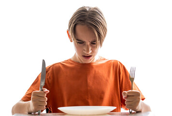 Upset little boy waiting for dinner while holding a fork, spoon. Hungry boy. Angry hungry boy child waiting for dinner. Holding fork and knife in his hands. Little boy sits in front of an empty plate