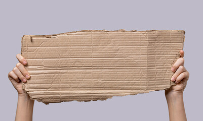 Close up hand holding an empty cardboard sign. Hand raised up and holding a blank piece of...