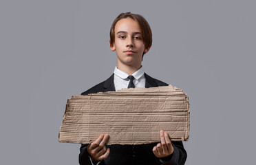 Serious child in suit with blank banner ad. Child boy holding empty blank poster. Boy showing blank poster. Young man holding blank empty banner, gesture looking serious