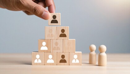 Hand placing person icon block atop pyramid of wooden blocks, two figurines beside structure.
