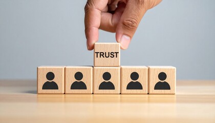 Five wooden blocks on wood surface, hand placing “TRUST” block atop center figure icon.