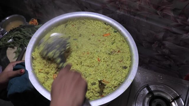A home-style preparation of rice pulao captured in warm, detailed footage, showcasing the mixing of spices, vegetables, and aromatic rice.