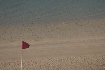 red flag on beach on sea or ocean as a symbol of danger. The sea state is considered dangerous and...
