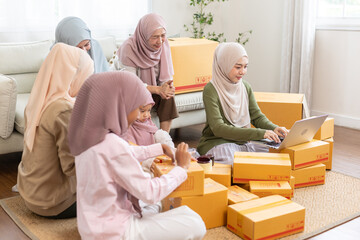 Smiling Muslim women working together on online business at home, packing parcels with laptop. Concept of female teamwork, e-commerce startup, digital business and family support.