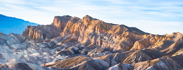 Sunrise at Zabriskie Point, Death Valley, California, golden sunlight shining on mountains