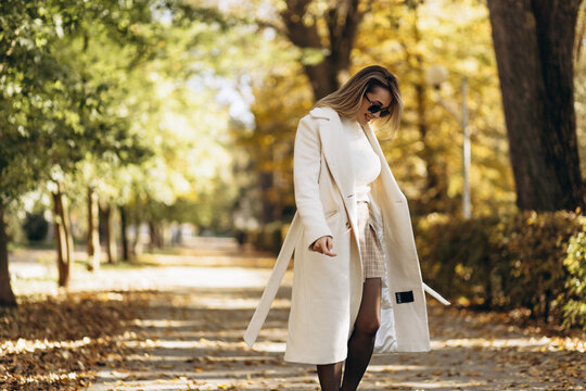 Young woman wearing coat and sunglasses walking in an autumn park - Powered by Adobe