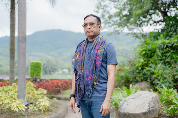 Mature Asian Man in Glasses and Scarf Standing in a Green Park