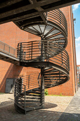 Black metal spiral staircase against a detailed red brick wall in Hamburg's port district.