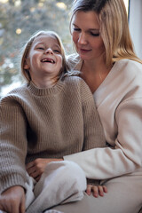 Woman and child, both in cozy knitwear, share a joyful moment indoors, surrounded by soft natural light, embodying warmth and connection in a serene atmosphere