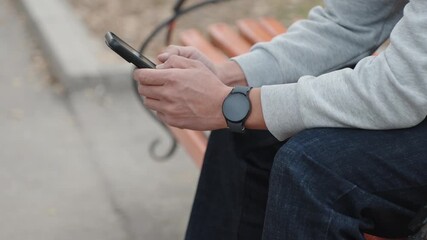 Sport person sits on bench in public park engaging with his smartphone. Jogger making notes about exercises in his gadget. Side view of tourist sitting on bench wearing dark modern smart watch. - Powered by Adobe