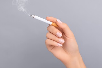 Elegant female hand with manicured nails holding a cigarette, wisps of smoke rising against a soft gray background, conveying a sense of relaxation and contemplation