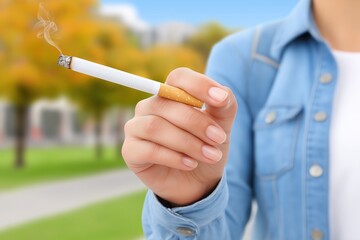 Woman holding a cigarette with smoke rising, dressed in a denim jacket, standing in a park with colorful autumn trees in the background, capturing a moment of relaxation