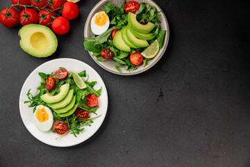 Avocado salad arugula, egg, tomato, mixed greens, vegetables dish fresh delicious gourmet food background tabletop rustic food top view copy space keto and paleo diet vegetarian food