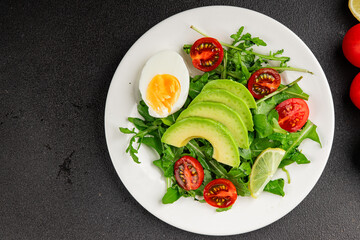Avocado salad arugula, egg, tomato, mixed greens, vegetables dish fresh delicious gourmet food background tabletop rustic food top view copy space keto and paleo diet vegetarian food