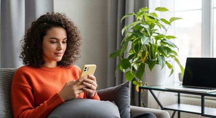 Young woman interacts with smartphone device in cozy interior setting while relaxing
