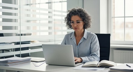 Professional woman working on laptop in bright office with natural light and focused expression