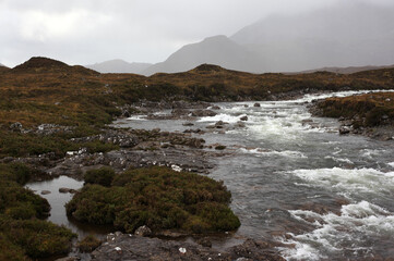 Scottish mountain loch in autumn surrounded by mountain peaks and rugged slopes, with water reflecting the dramatic highland landscape in Scotland