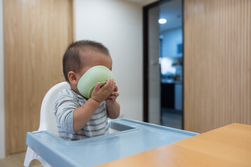 Adorable baby holding bowl during mealtime at table
