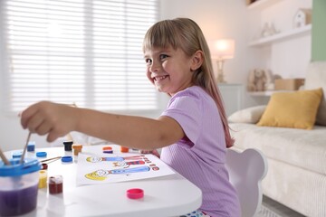 Little girl with brush drawing at white table indoors