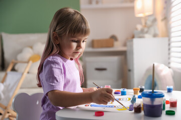 Little girl with brush drawing at white table indoors