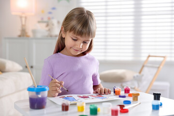 Little girl with brush drawing at white table indoors