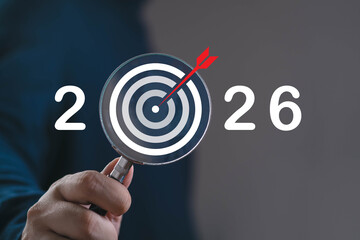Hand holding a magnifying glass highlighting a target with an arrow and the year 2026, symbolizing future goals, strategic focus, business planning, and long-term vision for upcoming achievements.