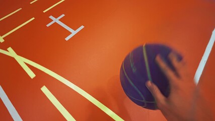 Point-of-view shot of person dribbling basketball on brightly lit indoor court with vivid orange flooring and white markings. Handheld real-time action camera footage - Powered by Adobe