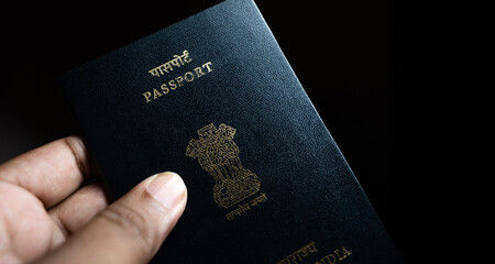 A person holds an Indian passport against a dark background, highlighting the cover’s golden...