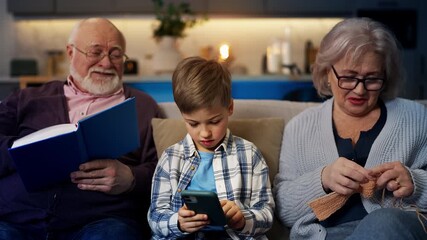 Grandpa and granny knitting and reading a book while little boy playing on phone - Powered by Adobe