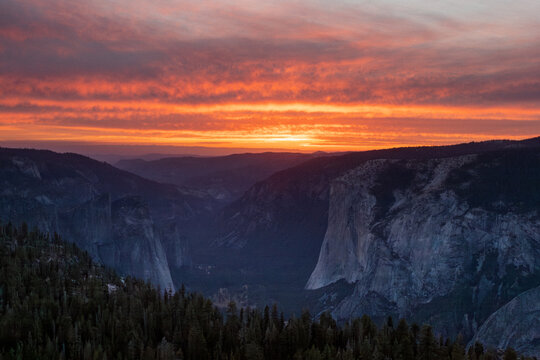 A vibrant sunset bathes the cliffs and a shadowed Yosemite Valley in warm, glowing light.