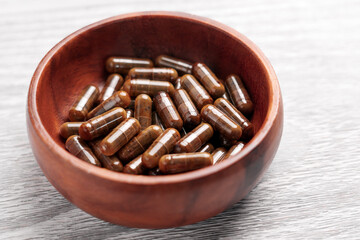 Brown medicinal capsules. Pills with herbal extracts in wooden bowl