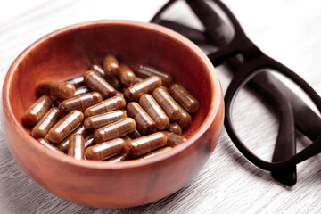 Rustic wooden bowl with brown herbal medicinal capsules on table