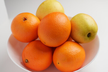 Fresh oranges and apples in ceramic bowl on white table