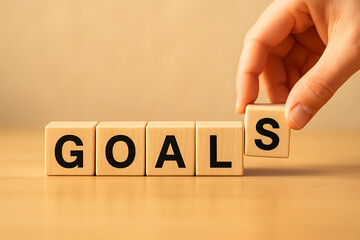 A hand is completing the word "goals" with a wooden block, signifying the importance of setting clear objectives and milestones in business or personal life for success