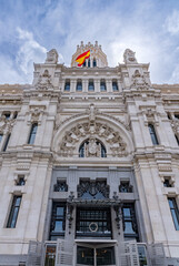 A detail of the Palacio de Cibeles' central entrance, showcasing its intricate Neo-Gothic style, stone arches, coat of arms, and detailed ironwork above the doorway