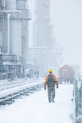 Fototapeta premium A worker navigates through heavy snowfall at an industrial site, showcasing resilience in harsh weather conditions.