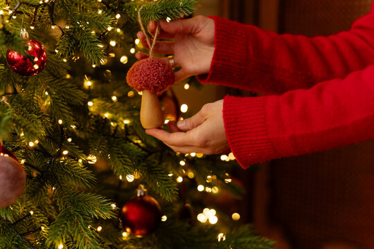 Close-up of a woman hanging a mushroom Christmas ornament on an illuminated Christmas tree