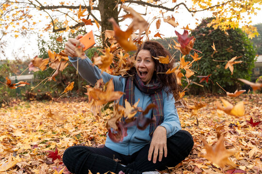 Woman feeling cheerful playing with falling autumn leaves and taking a selfie