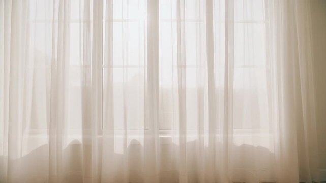 White sheer curtains gently moving by window with morning light