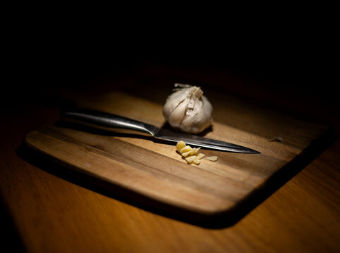 Close-up of a bulb of garlic on a wooden chopping board with a sliced clove of garlic